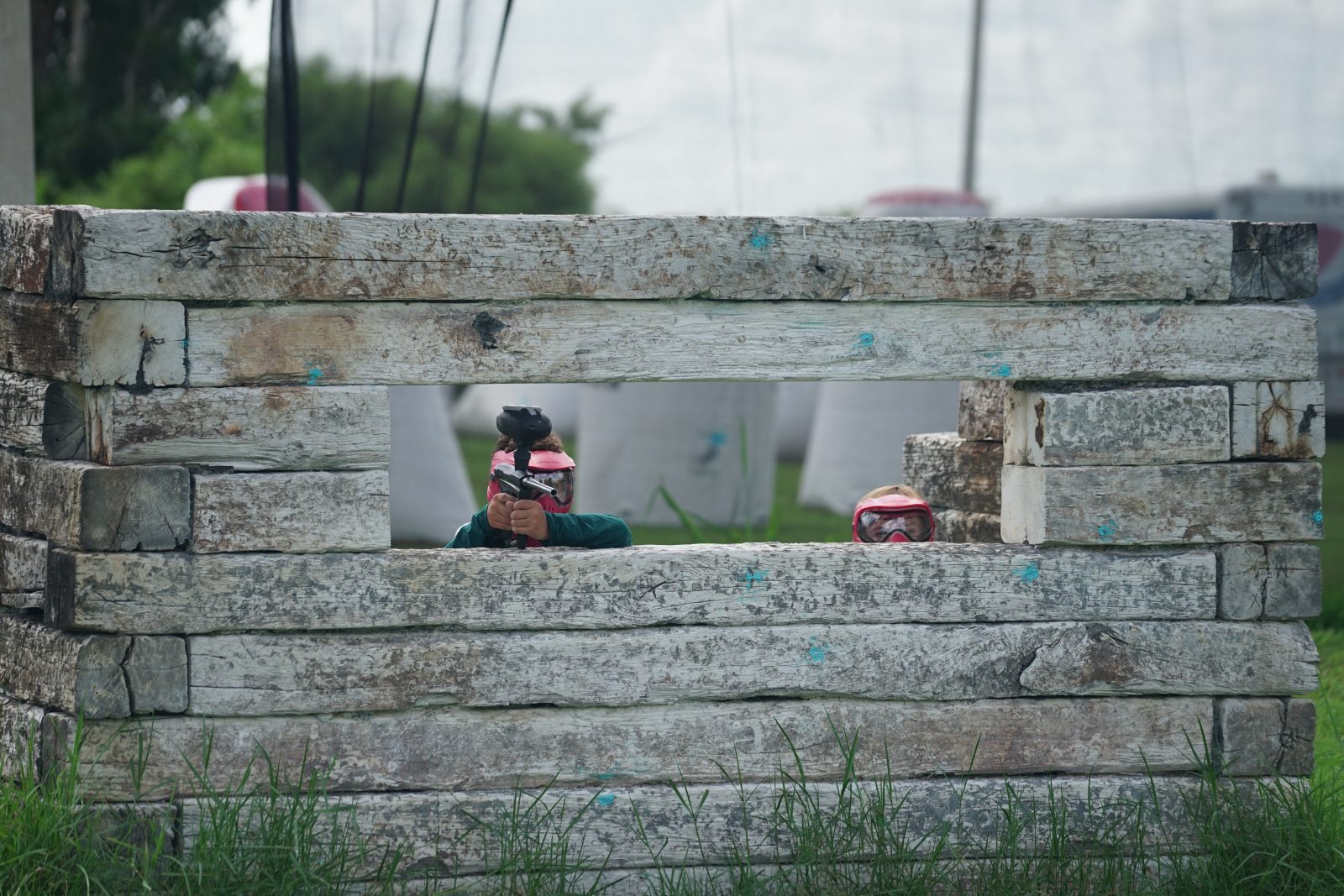 Paintball player taking aim through a wooden bunker at Fort Myers Paintball Park
